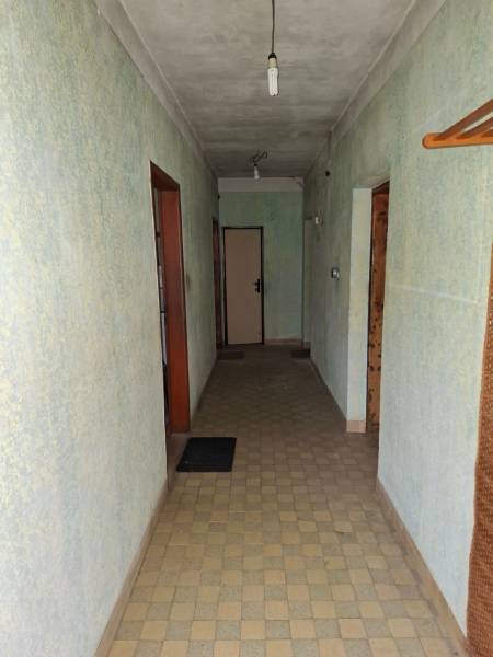 Chodba v rodinném domě se světle zelenými stěnami, dlažbou a jednoduchým osvětlením.