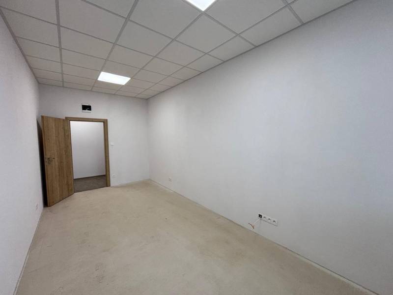 Interiér kanceláře s bílými stěnami, podhledovým stropem a otevřenými dveřmi.