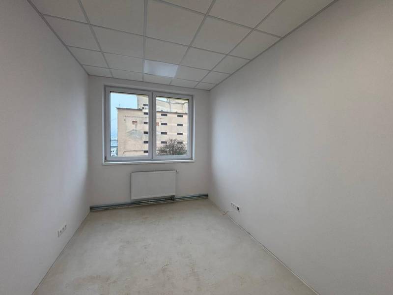 Bílá kancelář s radiátorem a výhledem z okna.