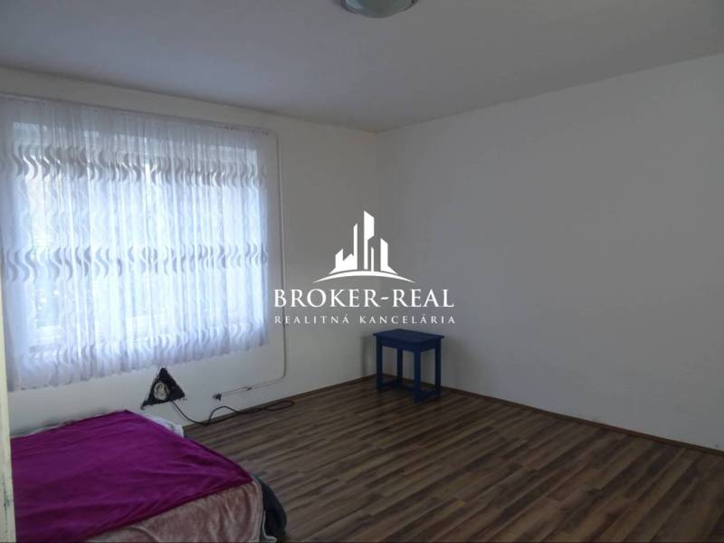 Pokoj s postelí, záclonami a podlahou s dřevěným dekorem v rodinném domě.