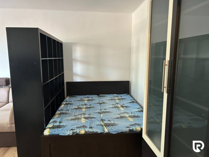 Ložnice v jednopokojovém bytě s postelí a úložnými skříňkami.