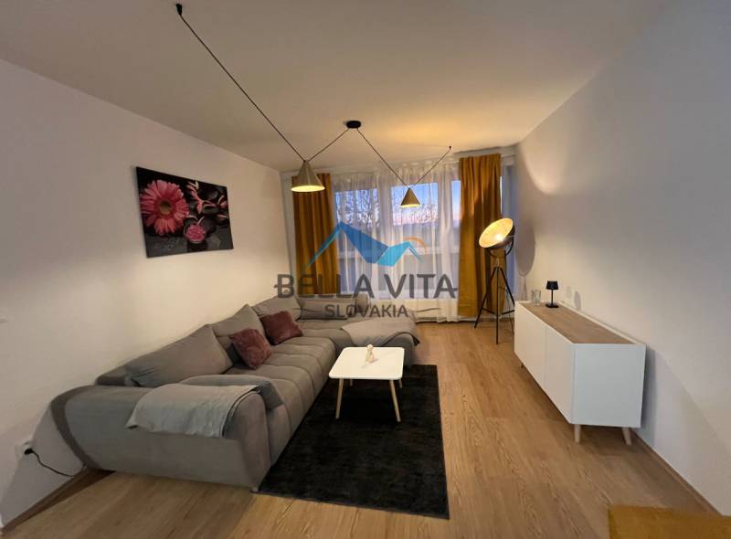 Obývací pokoj v 2pokojovém bytě s pohovkou a podlahou s dřevěným dekorem.