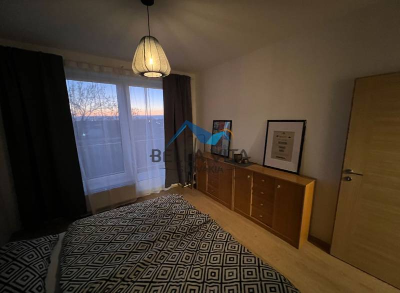 Ložnice s komodou a lampou, podlaha s dřevěným dekorem v dvoupokojovém bytě.