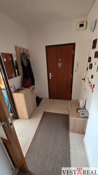 Chodba v 3-pokojovém bytě se světlým nábytkem a hnědými doplňky.