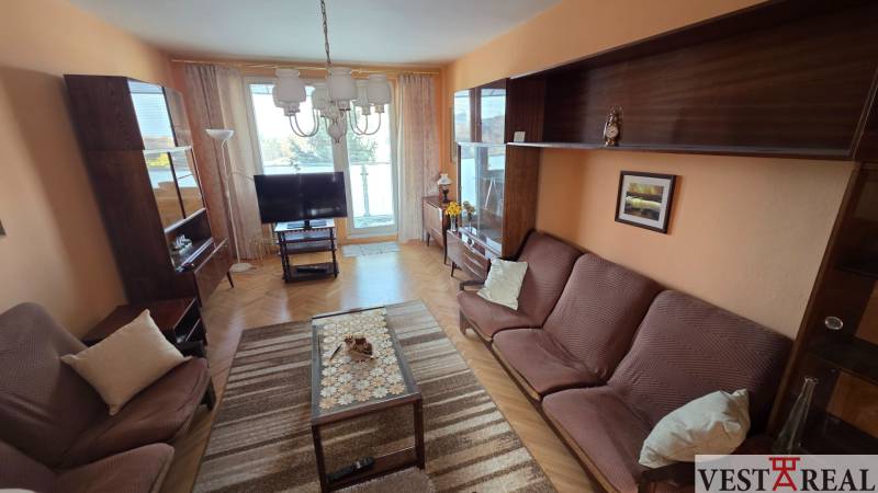 Obývací pokoj v 3-pokojovém bytě s pohovkami, skříněmi a podlahou s dřevěným dekorem.