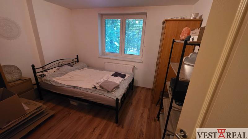 Ložnice ve 3-pokojovém bytě s kovovou postelí a podlahou s dřevěným dekorem.