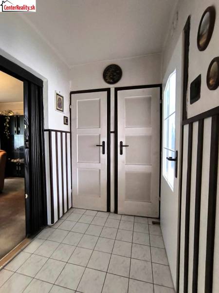 Interiér rodinného domu s bílými dveřmi, dlažbou a tmavým obkladem stěn.