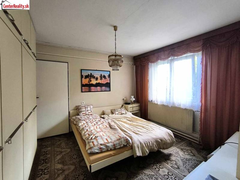 Ložnice v rodinném domě s postelí, skříní a obrazem na stěně.