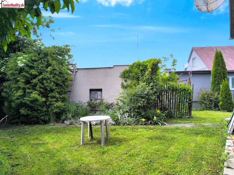 Zahrada rodinného domu v Novácích s trávníkem, stolkem a okrasnými keři.