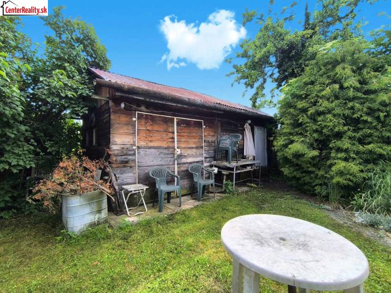 Dřevěná chatka s plastovými židlemi v zahradě rodinného domu v Novácích.