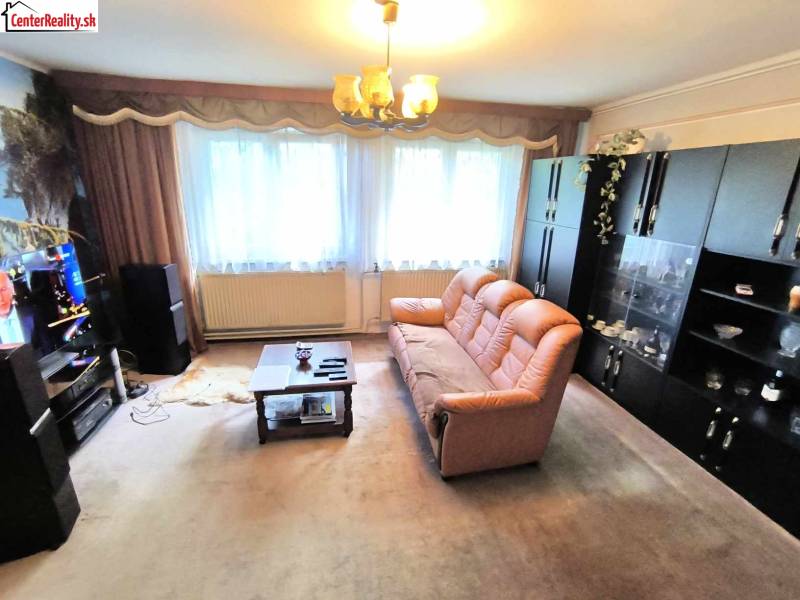 Obývací pokoj v rodinném domě s hnědou pohovkou, skříňkami a televizí na stěně.