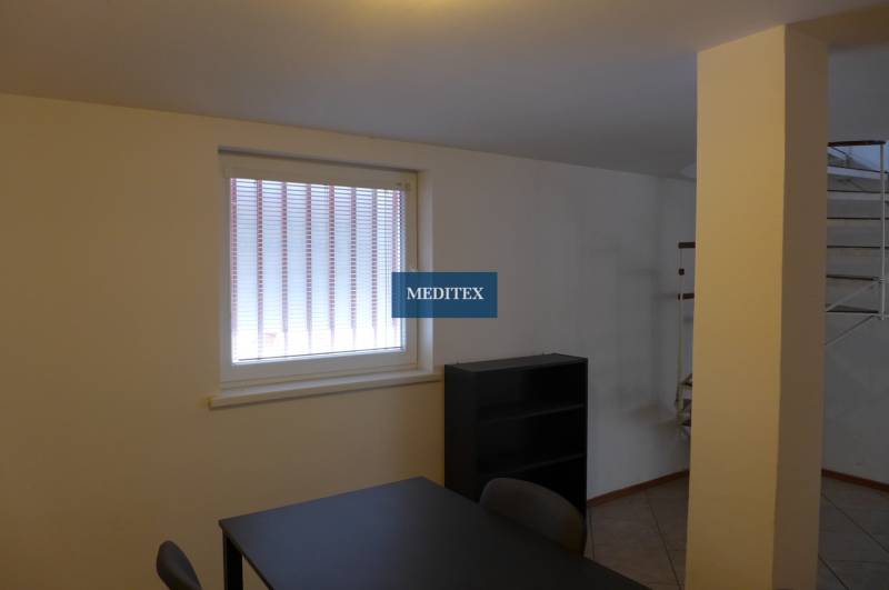 Kancelářský prostor se stolem a regálem, sklady a haly, světlá atmosféra.