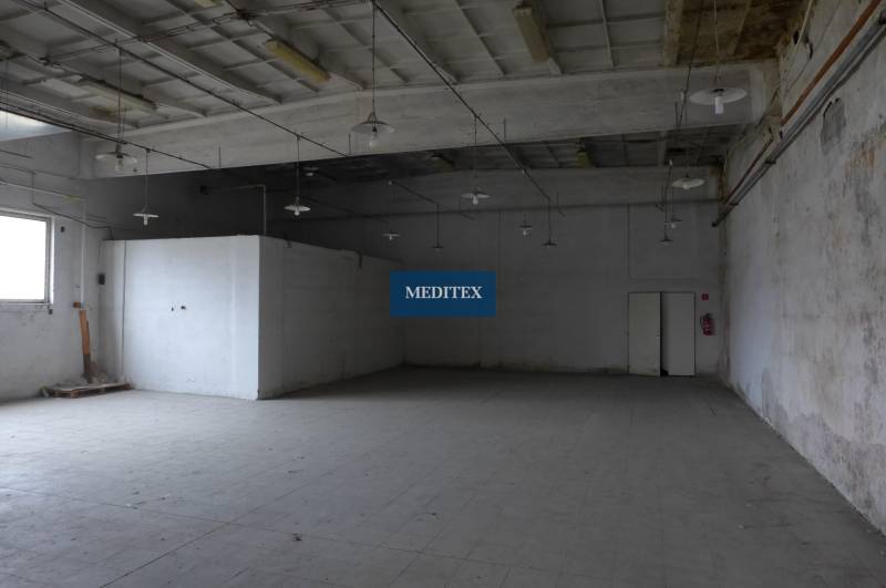 Průmyslový interiér skladu s vysokým stropem a betonovou podlahou.