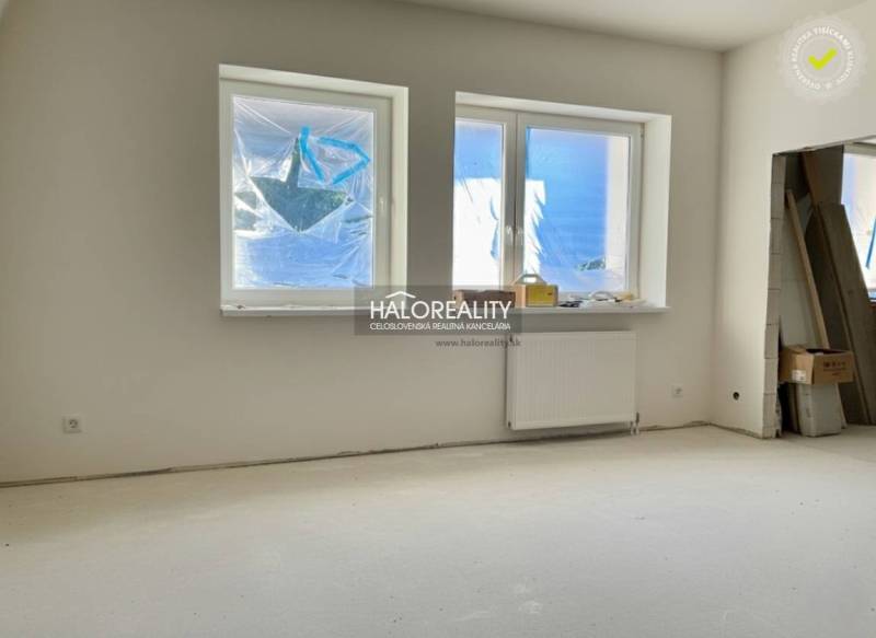 Pokoj v rodinném domě s okny a radiátorem, nevyužitý prostor připravený k dokončení.