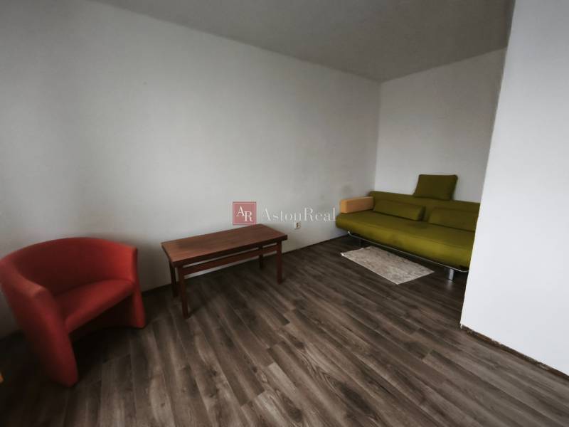 1-pokojový byt s podlahou s dřevěným dekorem, zelenou pohovkou a červeným křeslem.