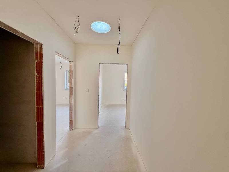 Chodba v rodinném domě s dočasným osvětlením a betonovou podlahou.