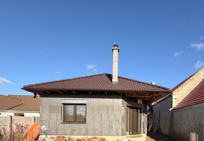 Rodinný dům v Cíferi ve výstavbě s hnědou střechou a komínem.