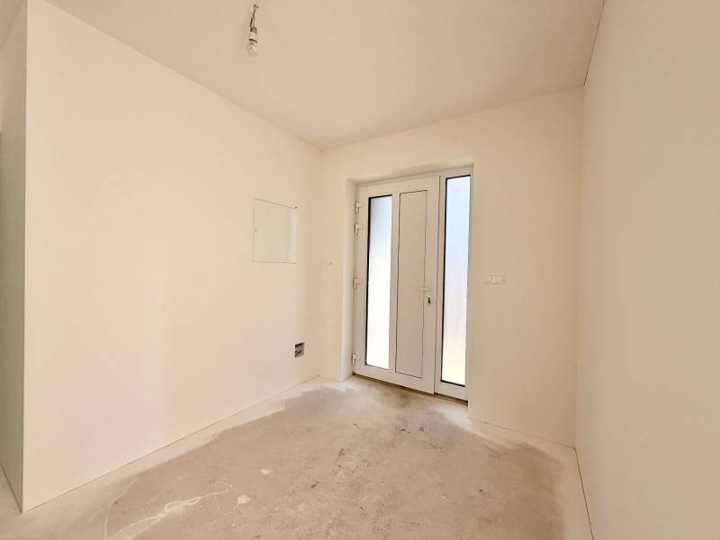 Prázdná místnost s francouzskými dveřmi v rodinném domě, bílé stěny, betonová podlaha.