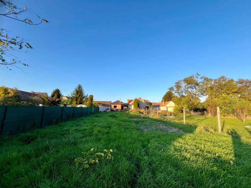 Pozemek s travnatým porostem a oplocením v Cíferu u rodinných domů.