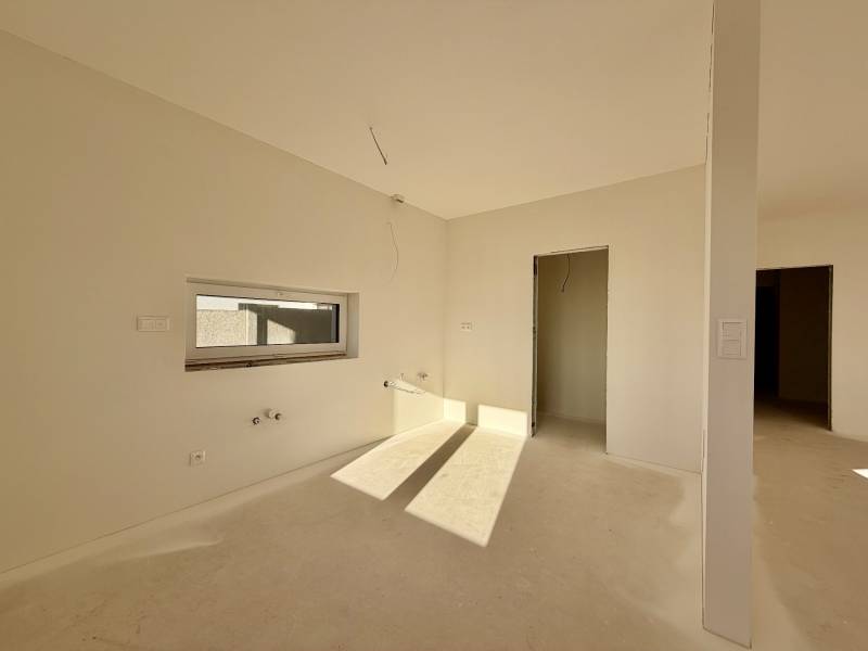 Prostorná nezařízená místnost v rodinném domě s oknem a dveřmi bez podlahy.