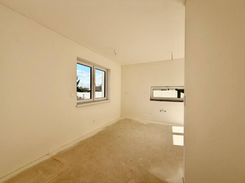 Prázdný pokoj s dvojitým oknem a betonovou podlahou v rodinném domě.