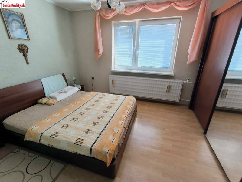 Ložnice v rodinném domě s postelí, skříní a podlahou s dřevěným dekorem.