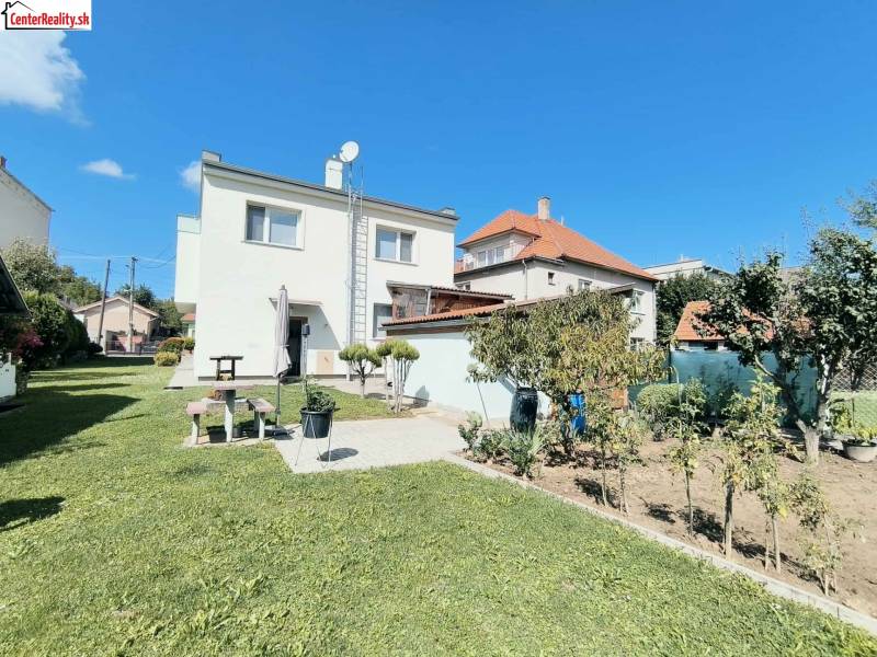 Rodinný dům v Partizánském obklopený zeleným trávníkem a zahradou pod modrou oblohou.