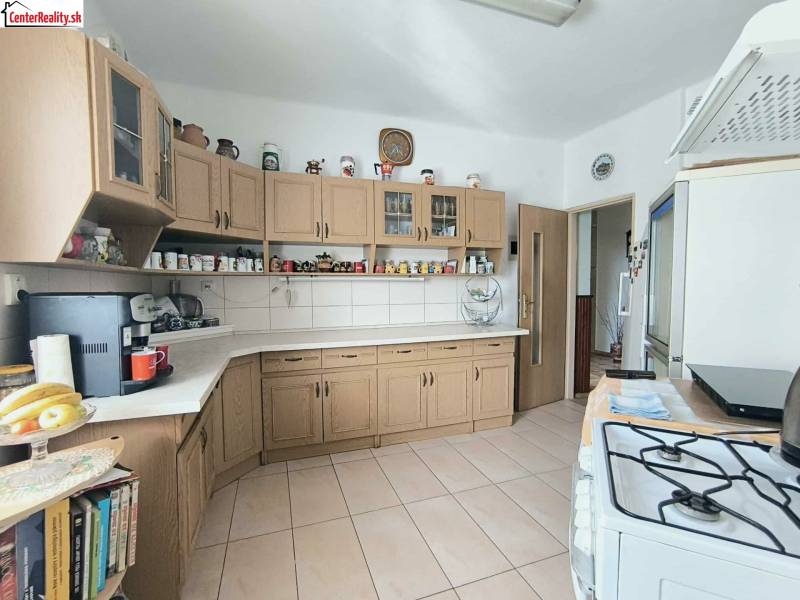 Kuchyně v rodinném domě s dřevěnými skříňkami a keramickou dlažbou.