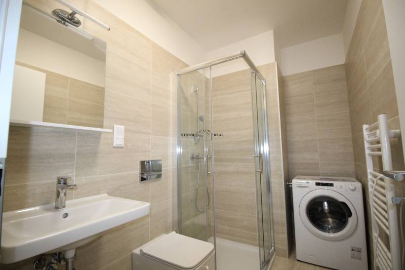 Koupelna v garsonce s umyvadlem, sprchovým koutem a pračkou.