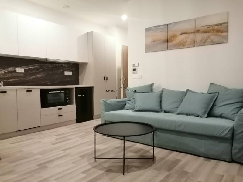 Garsonka s kuchyní, modrou pohovkou, kulatým stolkem a podlahou s dřevěným dekorem.