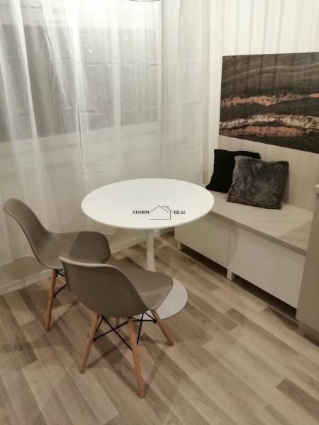 Jídelní kout s kulatým stolem, dvěma židlemi a dekoračními polštáři, podlaha s dřevěným dekorem.