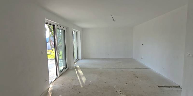 Prostorná místnost v rodinném domě s velkými okny a betonovou podlahou.