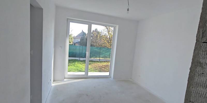 Bílá místnost s velkým oknem a výhledem na zahradu v rodinném domě.