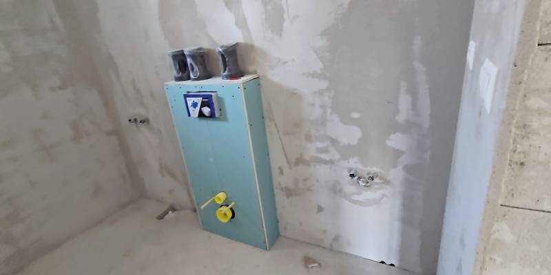 Nedokončená koupelna v rodinném domě s připravovanou instalací ve stěně.