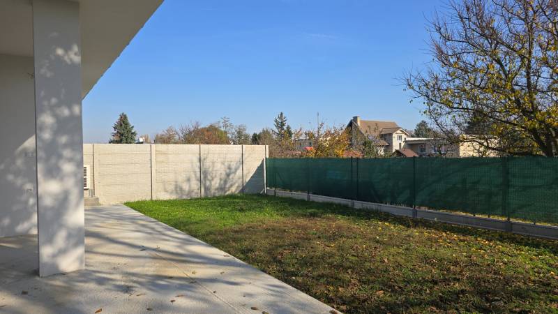Zahrada rodinného domu v Piešťanech s trávníkem, betonovou terasou a oplocením.