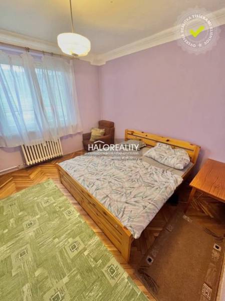 Ložnice ve 4pokojovém bytě s postelí, křeslem a podlahou s dřevěným dekorem.