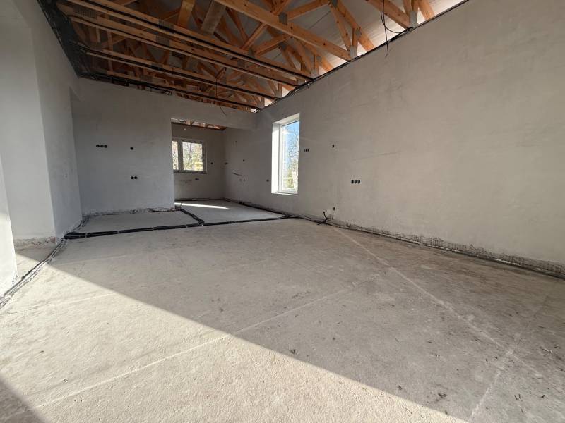 Interiér rodinného domu s betonovou podlahou, dřevěnými trámy a rozvody elektřiny.