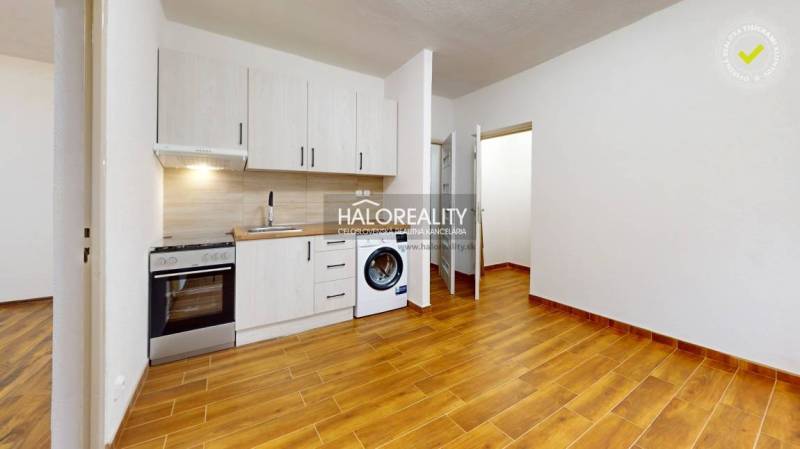 Kuchyně v 1-pokojovém bytě s podlahou s dřevěným dekorem a bílými skříňkami.