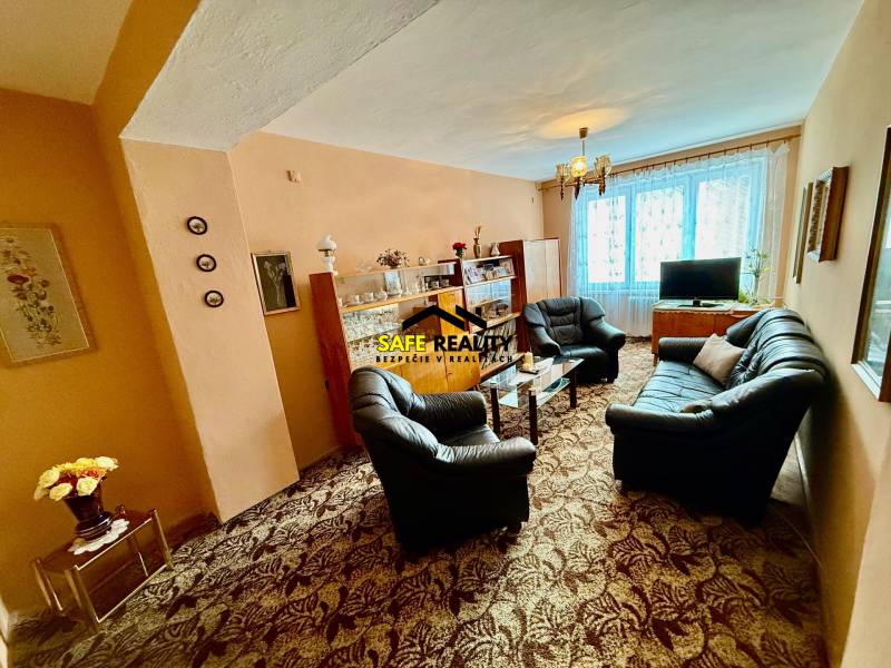 Obývací pokoj v 2-pokojovém bytě s pohovkou a prosklenou vitrínou.