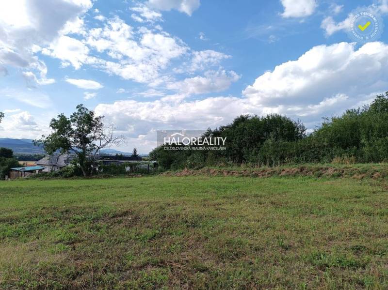 Pozemky - bydlení v Čerhově, travnatá plocha, stromy, vzdálené domy, kopce, modrá obloha.