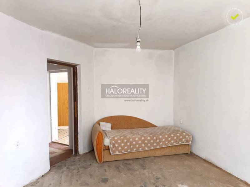 Interiér rodinného domu se starší pohovkou a surovou betonovou podlahou.