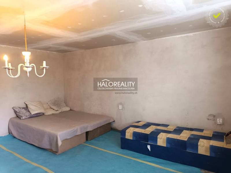 Ložnice v rodinném domě s postelí, matrací, svítidlem a jednoduchým nábytkem.