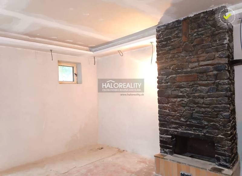 Interiér rodinného domu s kamenným krbem a malým oknem.