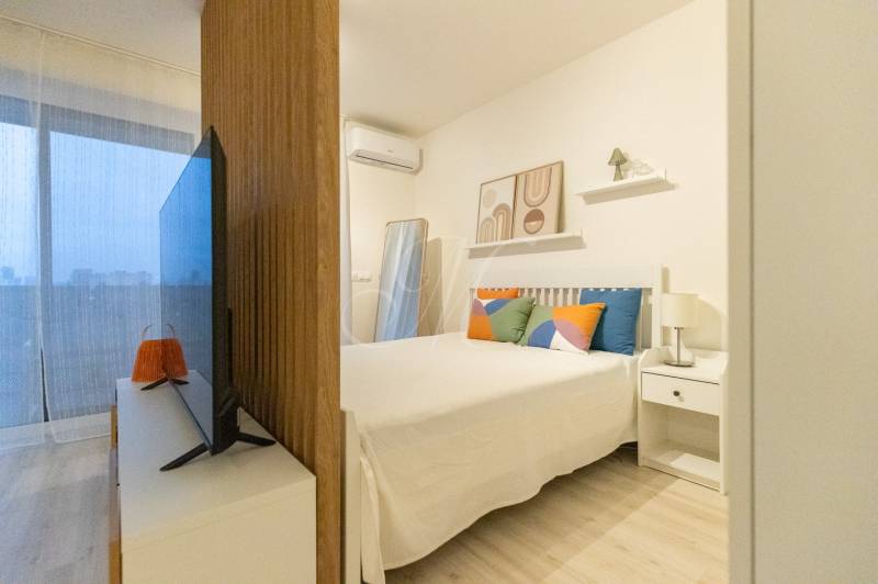 1-pokojový byt s postelí, televizorem a dekorativními polštáři. Podlaha s dřevěným dekorem.