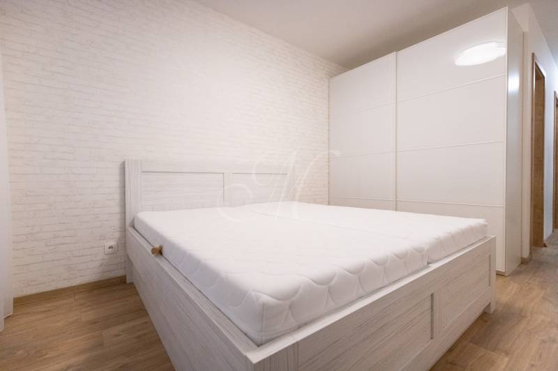 Světlá ložnice s bílou postelí, vestavěná skříň, podlaha s dřevěným dekorem v 2-pokojovém bytě.