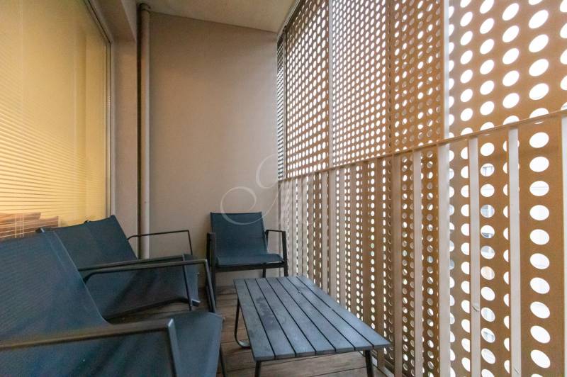 Balkon s dřevěným dekorem, posezením a perforovanou stěnou v 2-pokojovém bytě.