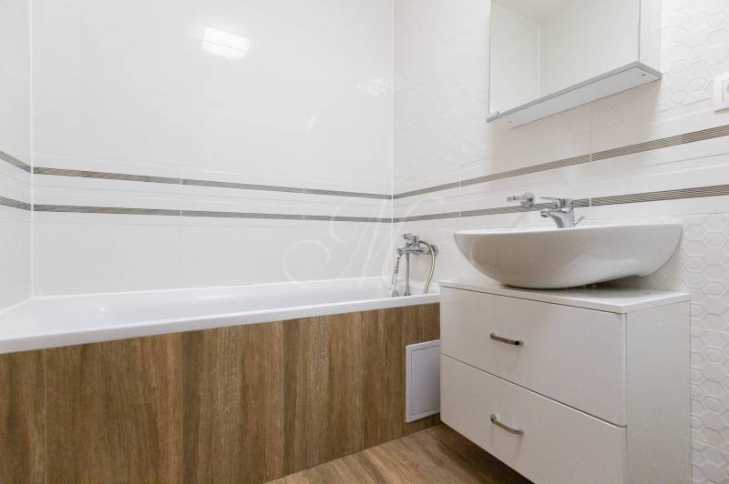 Koupelna v 2-pokojovém bytě s vanou, umyvadlem a podlahou s dřevěným dekorem.