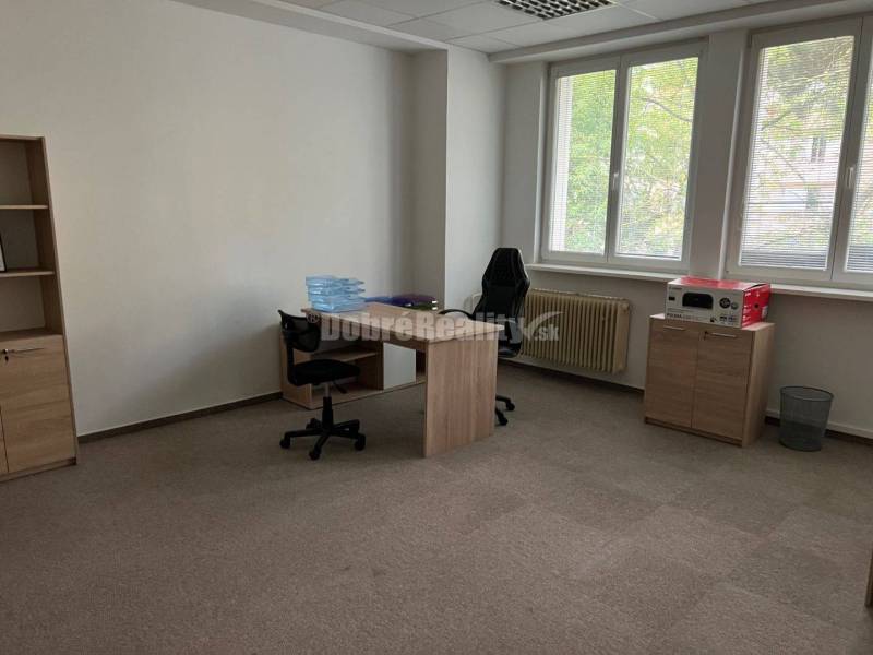 Kancelář s kobercovou podlahou, stoly, židlemi a regály v obchodních prostorách.