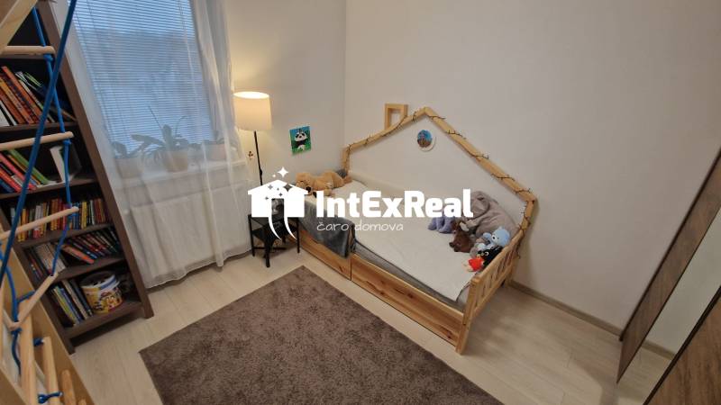 Dětský pokoj v 3-pokojovém bytě se světlou podlahou a poličkou plnou knih.