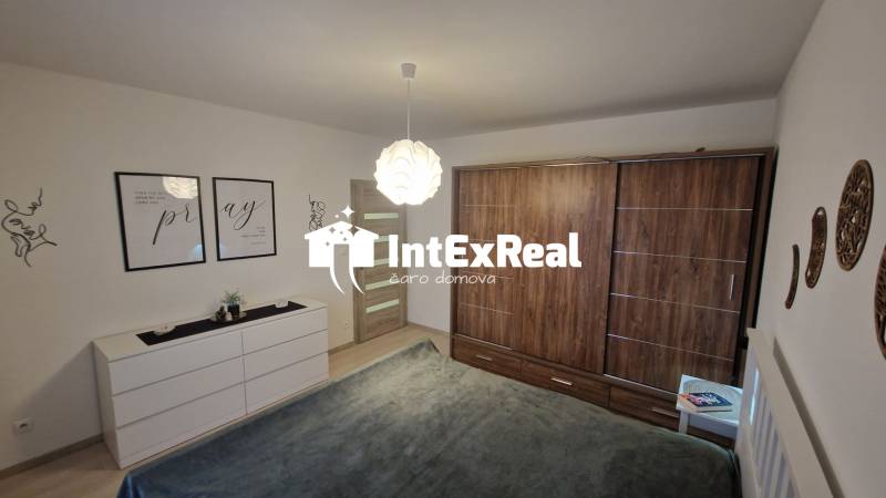 Ložnice ve 3-pokojovém bytě s podlahou s dřevěným dekorem, bílý nábytek, dekorace na stěnách.